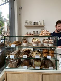 a man standing in front of a display case filled with cakes and muffins