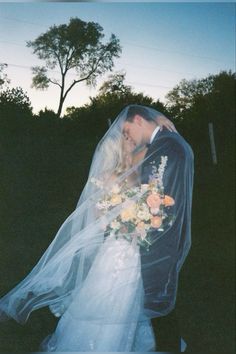 a bride and groom kissing under a veil on their wedding day in the evening sun