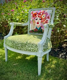 a green chair with a painting on it in the middle of some grass and flowers