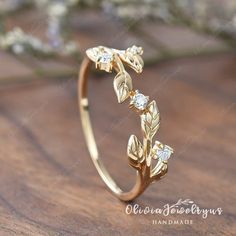 a gold ring with leaves and diamonds on it sitting on top of a wooden table