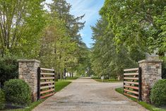 an entrance to a park with stone pillars and wooden gates, surrounded by green trees