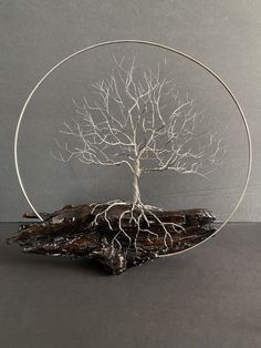 a wire tree sculpture on top of a piece of wood with roots growing out of it