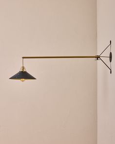 a lamp hanging from the side of a white wall next to a light fixture with a black shade on it