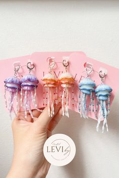 a hand holding five jellyfish earrings in different colors