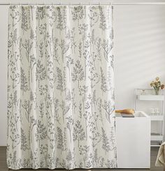 a white shower curtain with black and white flowers on it next to a bath tub