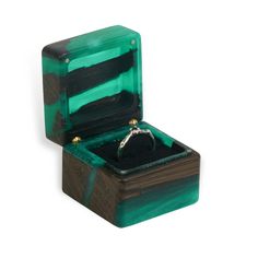 an open ring box with a green and black marble inside