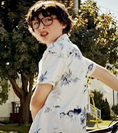 a young boy wearing glasses standing next to a bicycle in front of a tree and house