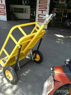 a yellow hand truck sitting on the side of a road next to a red scooter