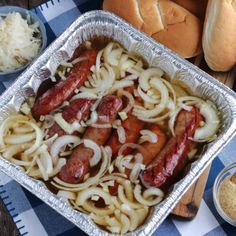 hot dogs and onions in a pan on a table with buns, gravy and bread