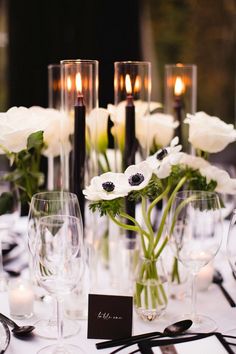 there is a table setting with white flowers and candles in vases on the table