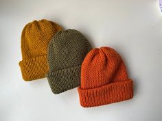 three knitted beanies sitting next to each other on a white surface, one is orange and the other is green