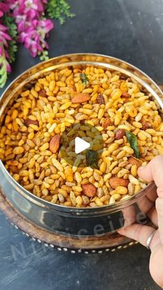 a person is holding a metal bowl filled with rice and other food on a table