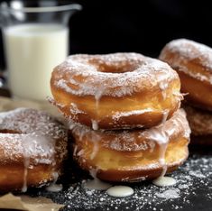 four donuts with icing and sugar sitting on a table next to a glass of milk