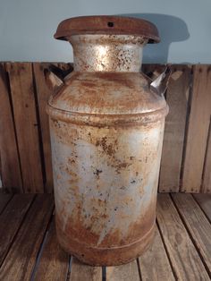 an old metal container sitting on top of a wooden floor next to a wall with wood planks