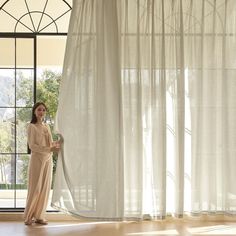 a woman standing in front of a window holding a blow dryer next to a curtain