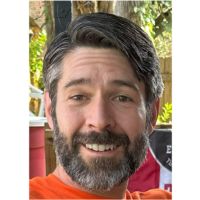 a man with a beard and orange shirt smiling at the camera while wearing an orange t - shirt