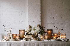 a table topped with plates covered in flowers and candles next to white brick wall behind it