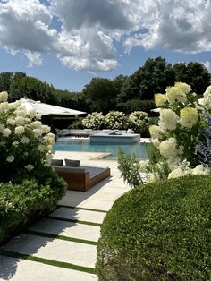 an outdoor patio with white flowers and greenery around the pool, surrounded by shrubs