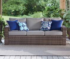 a couch with blue and white pillows on it in front of some potted plants