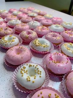 many pink and white cupcakes with sprinkles on them sitting on a table