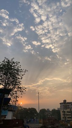 the sun is setting behind some clouds in the sky over a city street with buildings and trees