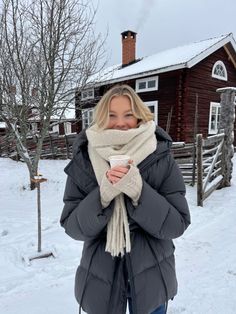 a woman standing in the snow with her scarf around her neck and holding a cup