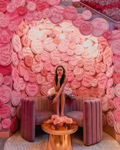 a woman sitting on top of a couch in front of a wall covered with hearts