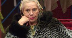 an older woman sitting on a red couch wearing a fur coat and looking at the camera