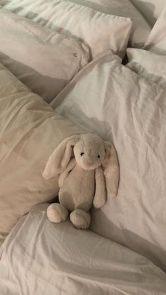 a stuffed animal sitting on top of a bed covered in white sheets and linens