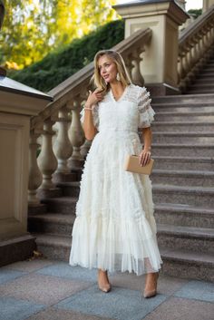 a woman in a white dress standing on some stairs with her hand on her hip