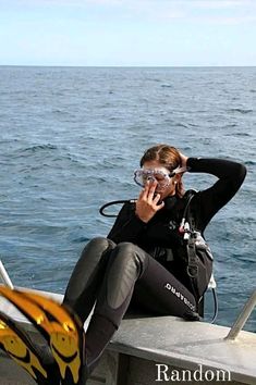 a woman in scuba gear sitting on the edge of a boat talking on her cell phone