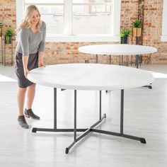 a woman standing next to a white table in an empty room with two round tables on each side