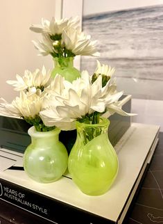 two green vases filled with white flowers on top of a book