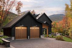 a black house with two garages and trees in the back ground, surrounded by fall foliage