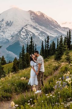 a man and woman standing on top of a lush green field next to a mountain