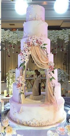 a wedding cake is decorated with flowers and ribbons on the top tier, as well as a bride and groom standing in front of it