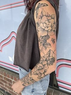 a woman with a flower tattoo on her arm standing in front of a brick wall