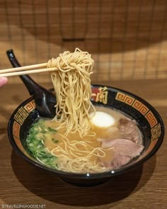 a person holding chopsticks over a bowl of ramen with meat and vegetables