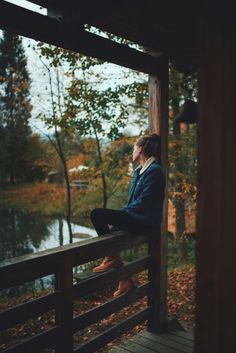 a person sitting on a wooden porch next to a body of water and some trees