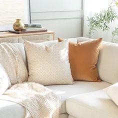 a white couch with several pillows on it in front of a window and a table