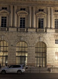 a white car parked in front of a tall building at night with people walking by