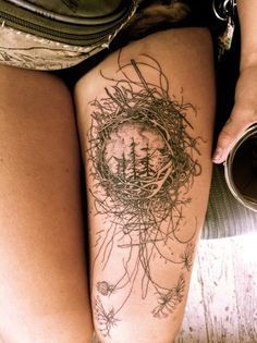 a woman's thigh with a bird nest tattoo on her left leg and pine trees in the background