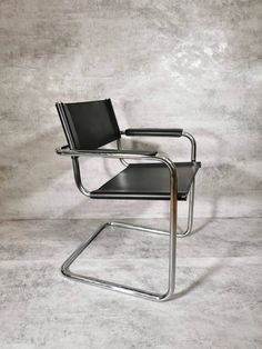 a black leather chair sitting on top of a white floor next to a gray wall