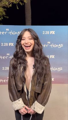 a woman with long hair standing in front of a sign and smiling at the camera