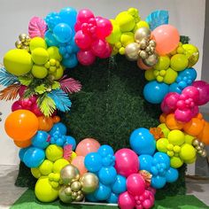 a wreath made out of balloons and greenery is displayed on a green carpeted floor