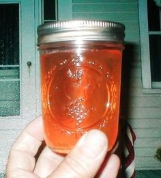 a hand holding a mason jar filled with orange liquid in front of a blue door