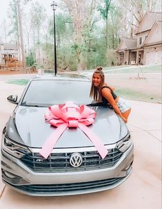 a woman sitting on the hood of a car with a pink bow