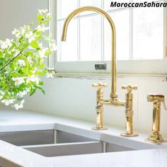 a white counter top with a gold faucet and sink in front of a window