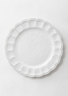 an empty white plate with scalloped edges on a plain surface, top view