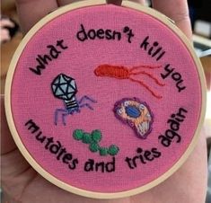 a hand holding a pink embroidered hoop with words and pictures on it that says, what doesn't kill your mates and tress